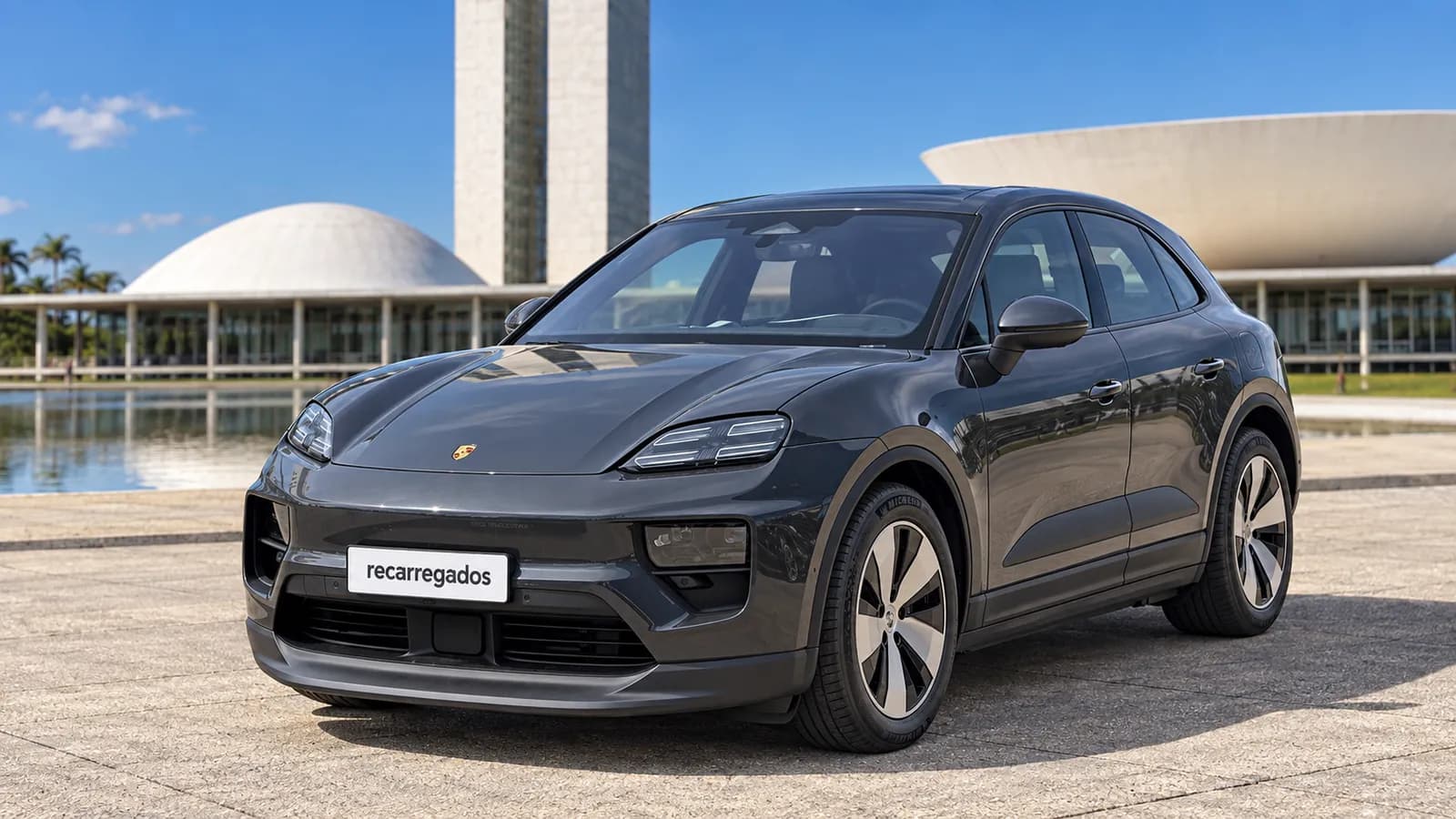 Porsche Macan Electric cinza-escuro diante da arquitetura modernista de Brasília, imagem gerada com IA a partir de foto real